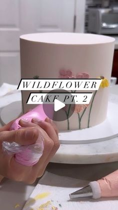 someone is decorating a cake with pink icing and flowers on the frosting