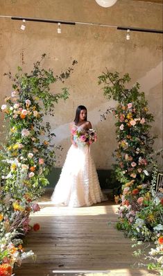 a woman in a wedding dress is standing under an archway with flowers and greenery