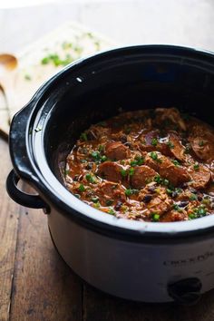 a close up of a stew in a crock pot on a wooden table next to a spoon