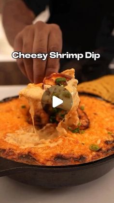 a person dipping some food into a skillet on top of a table with the words cheesy shrimp dip