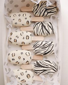 several popsicles decorated with animal print and wooden sticks in a white box on a polka dot tablecloth