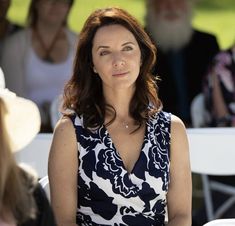 a woman sitting at a table with people in the background looking up and to her left