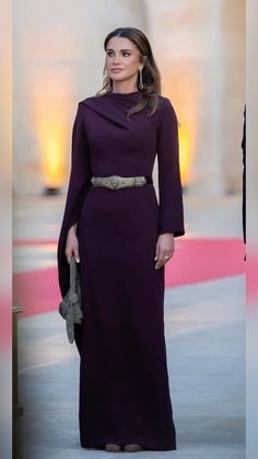 a woman in a long purple dress is standing outside