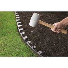 a person holding a hammer over the top of a garden bed with dirt and grass