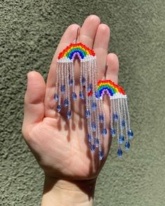 a person's hand holding two rainbow earrings