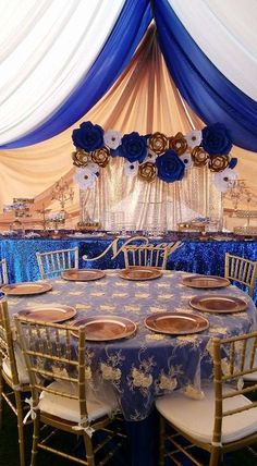 a banquet table set up with blue and white linens, gold plates and flower centerpieces