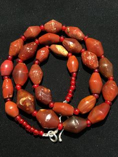 a red beaded necklace with orange and brown beads on a black surface, next to a silver clasp