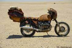 a motorcycle parked on top of a dirt field in the middle of nowhere with luggage strapped to it's back