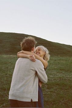 a man and woman hug each other while standing in front of a grassy hill on a sunny day