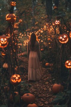 a woman in a white dress is walking through the woods with pumpkins all around her