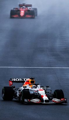 two red and white racing cars driving on a race track in the foggy weather