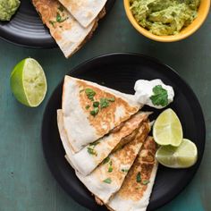 three quesadillas with guacamole and limes on the side