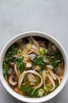 a white bowl filled with soup and vegetables on top of a gray countertop next to a spoon