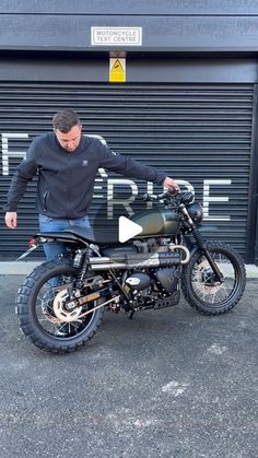 a man standing next to a motorcycle in front of a garage door with the words ride written on it