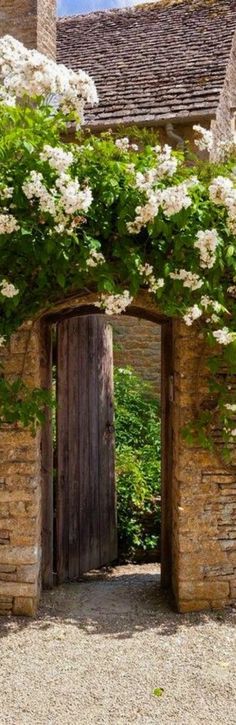 an old stone building with white flowers growing on it's sides and doors open