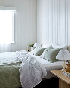 a bed with white sheets and green pillows in a bedroom next to a lamp on a table