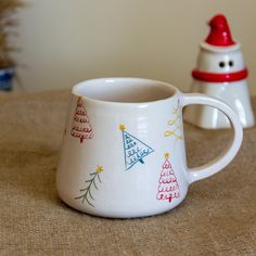 two coffee mugs sitting on top of a table next to a small christmas tree