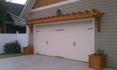 a white garage with a wooden pergolan attached to the roof and two planters in front of it