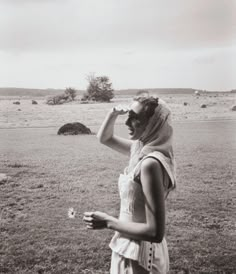 a woman standing in the middle of a field drinking from a bottle and looking into the distance