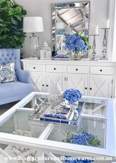 a living room filled with furniture and blue flowers on top of a glass coffee table