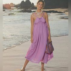 a woman in a purple dress standing on the beach with her handbag and purse