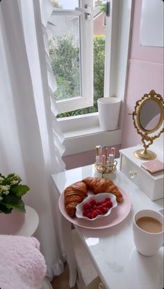 two croissants on a pink plate with raspberries in front of a window