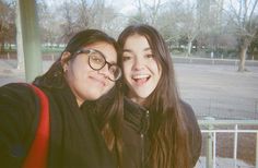 two young women taking a selfie in front of a metal fence at a park