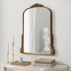 a mirror sitting on top of a white table next to a candle and some books