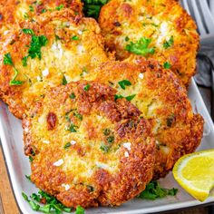 three crab cakes on a white plate with lemon wedges and parsley garnish