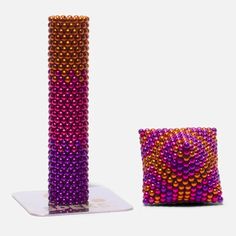 a purple and orange beaded vase next to a square shaped object on a white surface