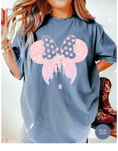 a woman wearing a blue shirt with minnie mouse ears on the front and castle in the back