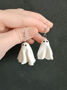 a pair of white ghost earrings hanging from a persons hand on a black background,