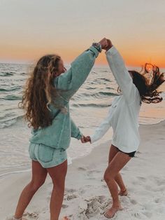 two women holding hands and dancing on the beach at sunset or sunrise with their arms in the air