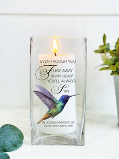 a glass candle with a hummingbird on it next to a potted green plant