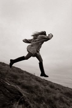 a woman jumping up into the air on top of a grass covered hill in black and white