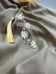 a glass bookmark with daisies and hearts on it sitting on a gray fabric