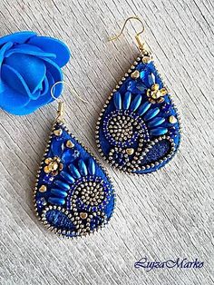 a pair of blue earrings sitting on top of a wooden table next to a flower