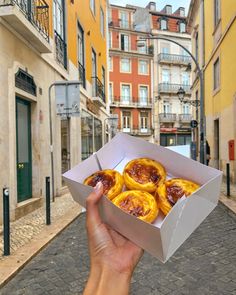 a hand holding up a box filled with pastries on a cobblestone street