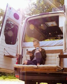 a man sitting in the back of a truck holding a camera and looking at his cell phone