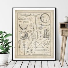 a framed poster with an old fashioned kitchen utensil diagram on the wall next to a potted plant