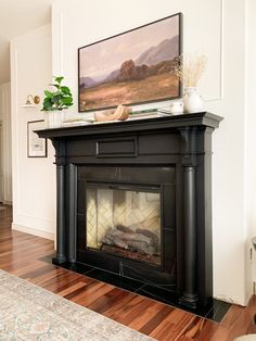 a fireplace in a living room with a painting on the mantle and hardwood flooring