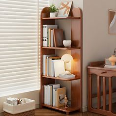 a wooden book shelf with books and other items on it next to a window covered in blinds