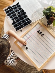 a young boy is writing on a piece of paper with letters and plants in the background