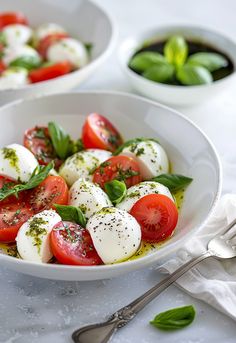 two white bowls filled with mozzarella and cherry tomatoes, garnished with basil