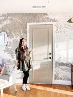 a woman standing in front of a door next to a wall with trees on it