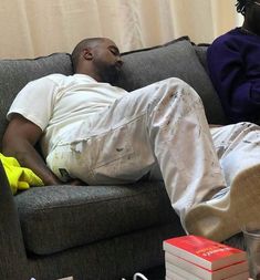 a man laying on top of a couch next to a pile of books