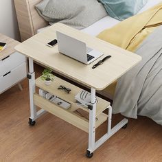 a laptop computer sitting on top of a wooden table next to a bed with pillows