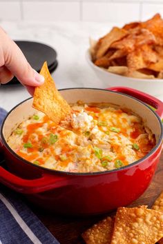 a hand dipping a tortilla chip into a bowl of cheesy dip