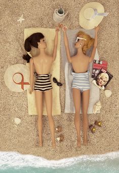 two dolls are laying on the beach with their arms in the air and one is wearing a bathing suit