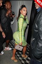 a woman in a tight green dress is standing near some people and taking pictures with her phone